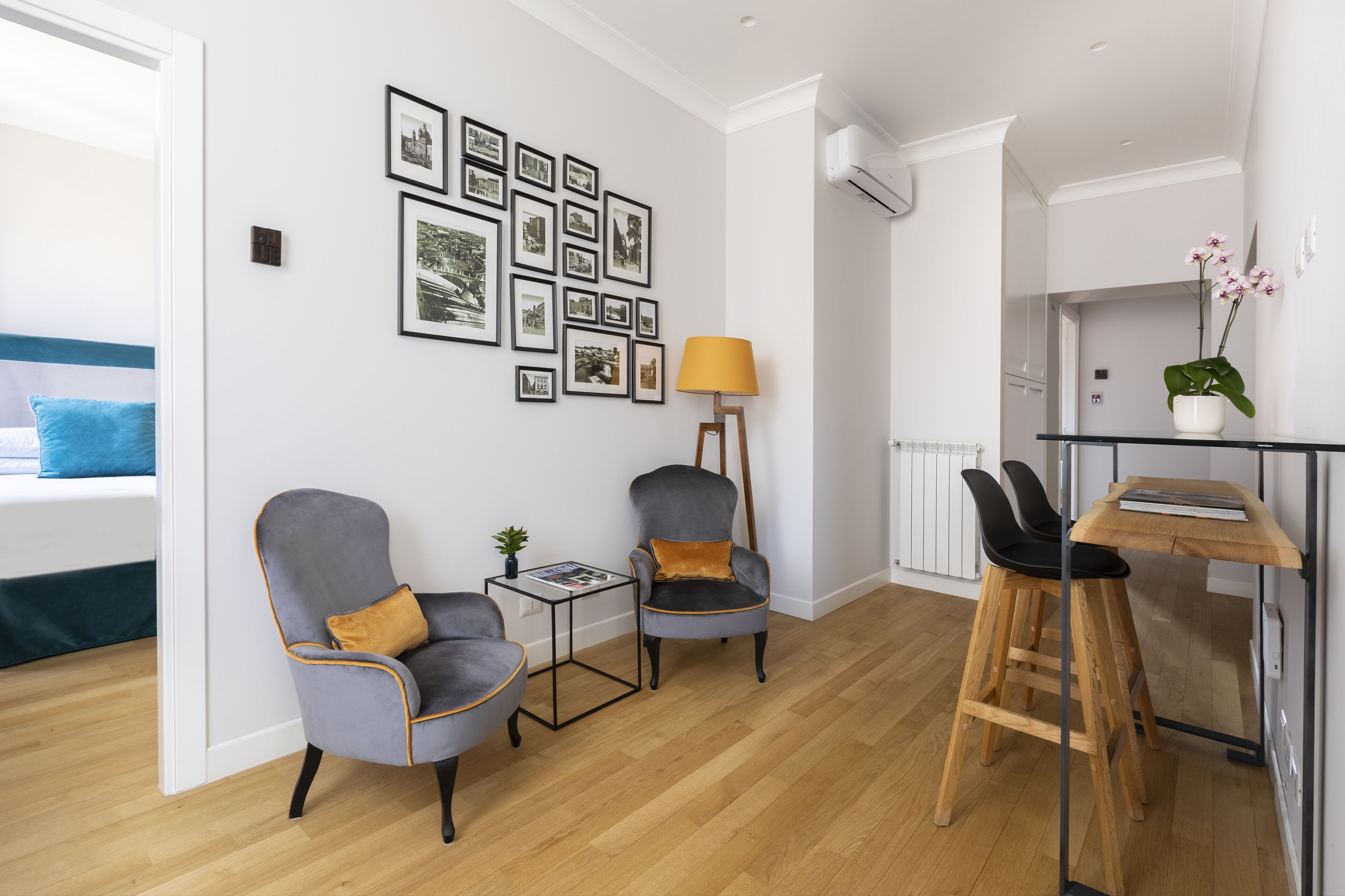A modern living room with a sofa, two armchairs, a small side table, a lamp, and a dining area with a wooden table and chairs.