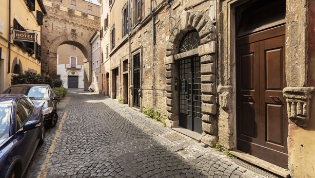 A cobblestone street with parked cars, a hotel sign, and an arched doorway. - Residenza Palline by Hili (Rome)