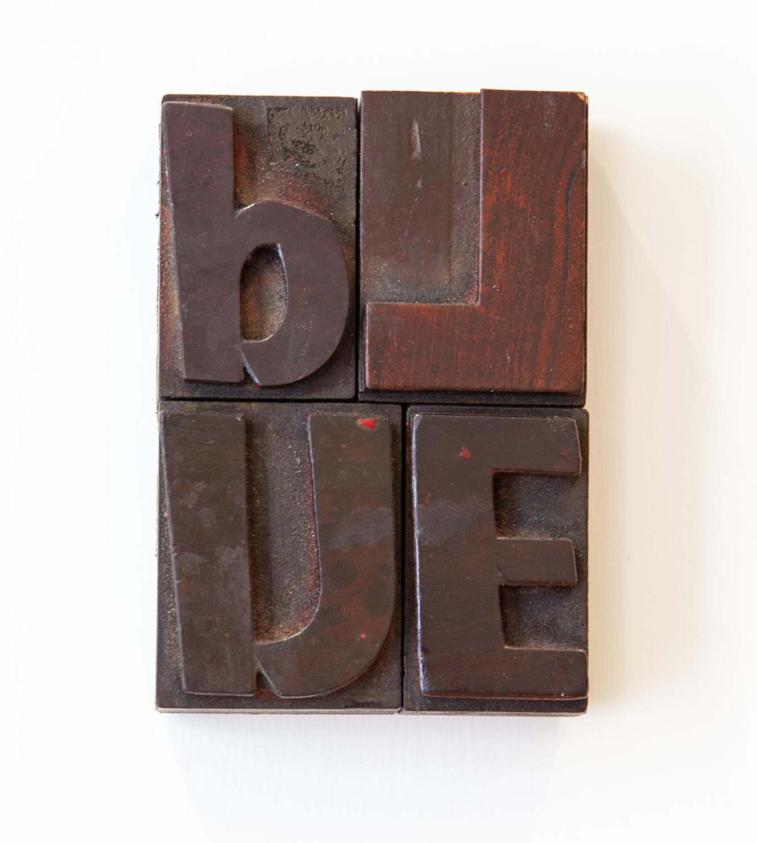 Un ensemble de quatre blocs de bois portant les lettres « b », « l », « u » et « e », disposés de manière à former le mot « BLEU ».