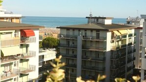A multi-story residential building with balconies, a clear view of the sea, and a rocky shoreline in the background. - Condominio Terme (San Michele al Tagliamento)