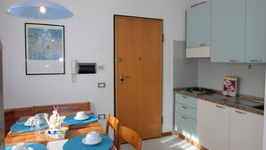 A dining area with a wooden table set for four, a blue pendant light, and a kitchen with light blue cabinets and a gas stove. - Condominio Terme (San Michele al Tagliamento)