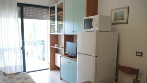 A compact kitchen with a microwave, refrigerator, and a small dining area with a table and chairs. - Condominio Terme (San Michele al Tagliamento)