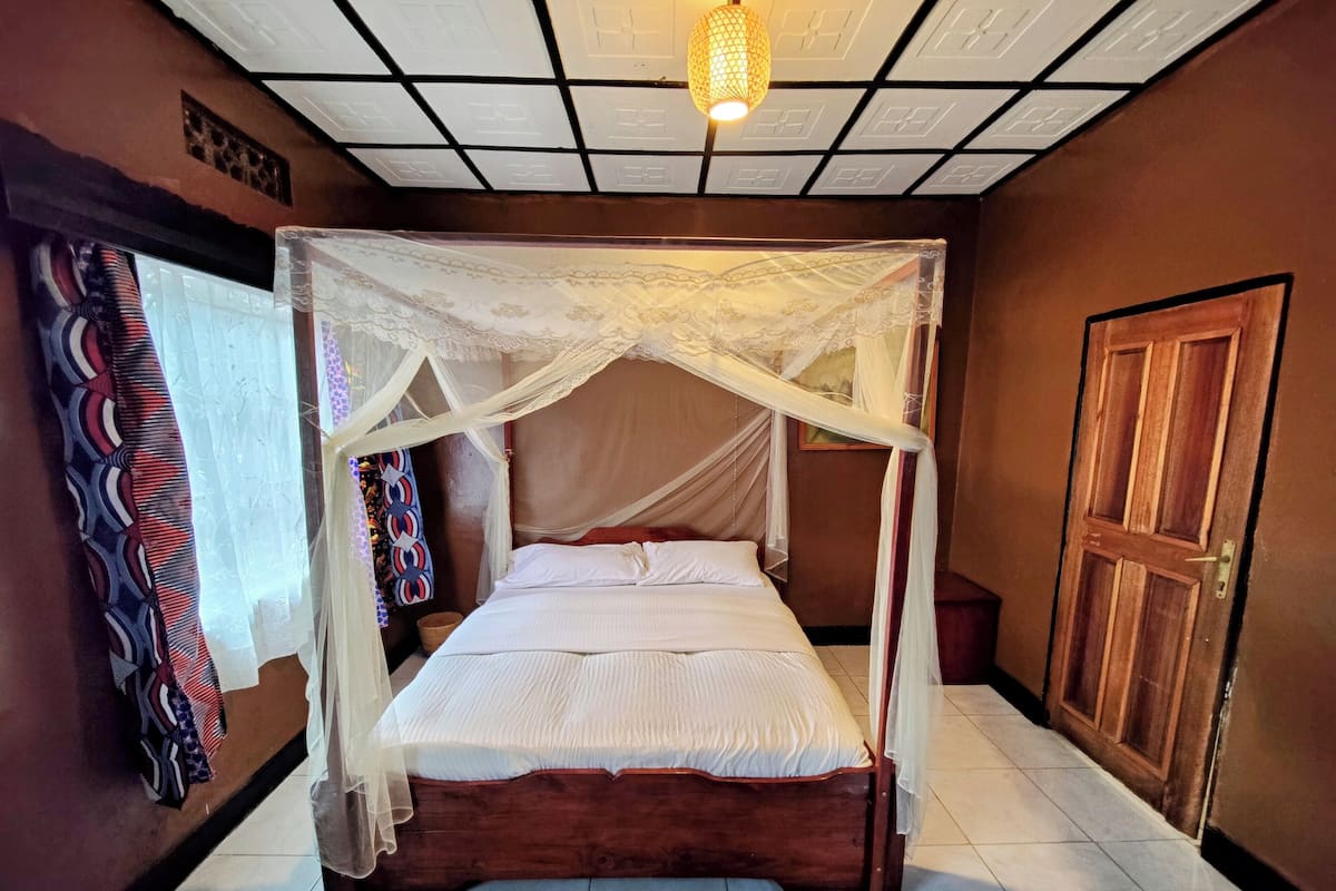 A four-poster bed with a canopy, a wooden door, and a tiled floor.