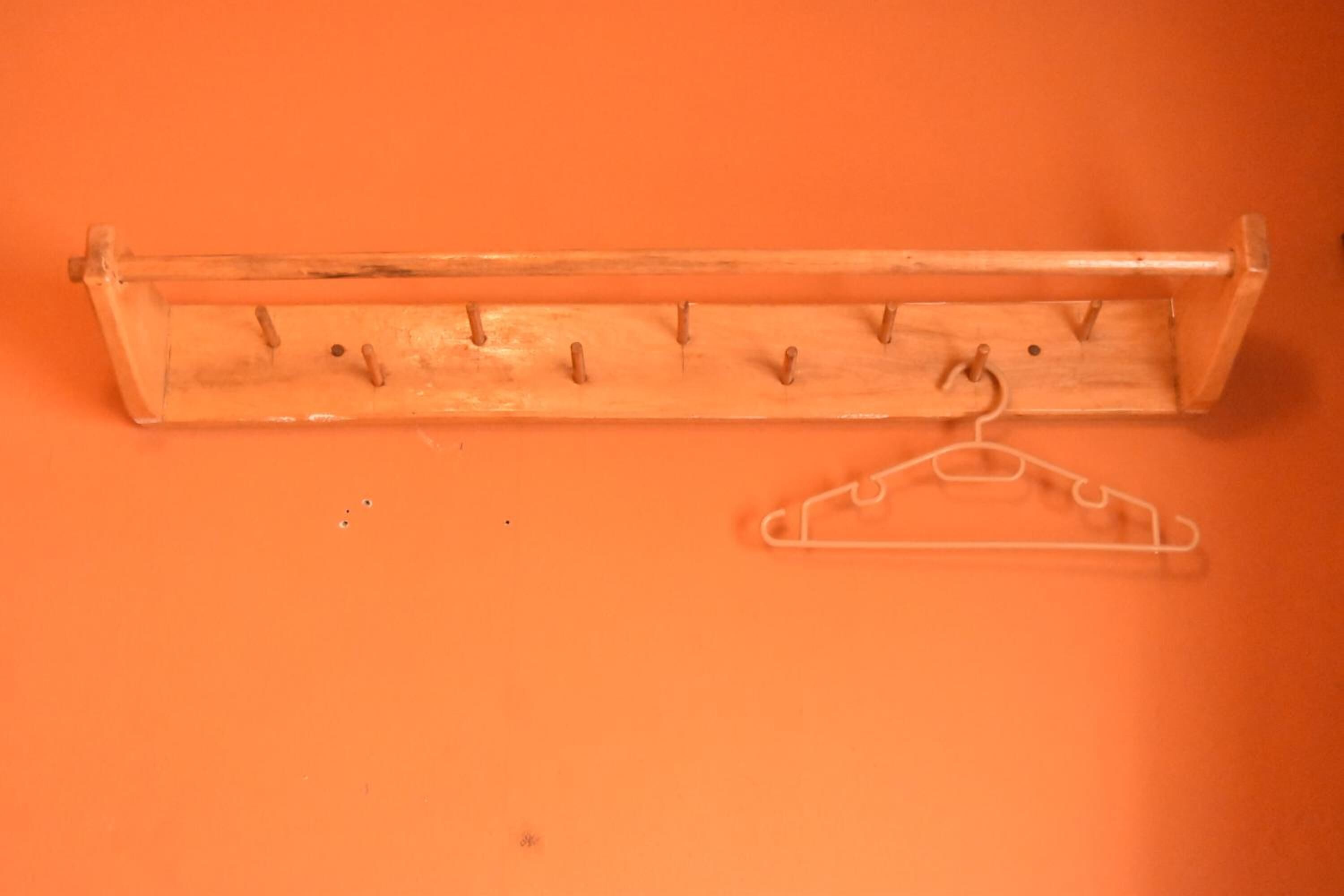 A wooden coat rack with hooks and a hanger against an orange background.