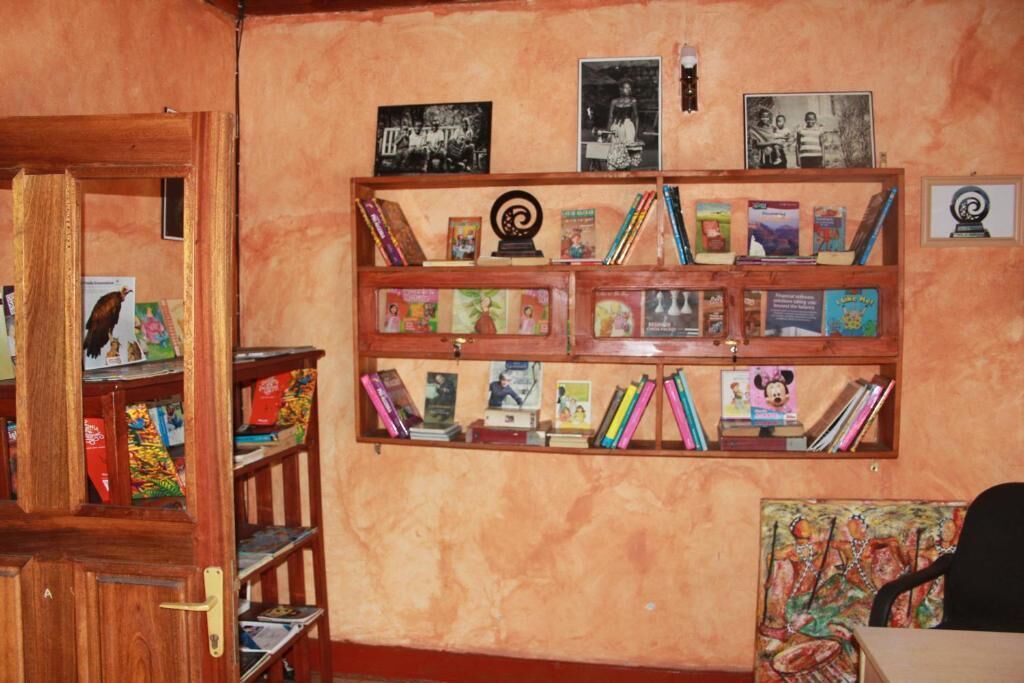 A room with a wooden bookshelf filled with books and framed pictures on the wall.