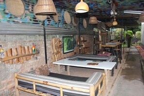 An outdoor seating area with tables and benches, a brick wall, and hanging lamps. - Amahoro Guest House (Muhoza)