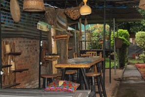 A rustic outdoor seating area with wooden tables and chairs, hanging baskets, and a brick wall. - Amahoro Guest House (Muhoza)