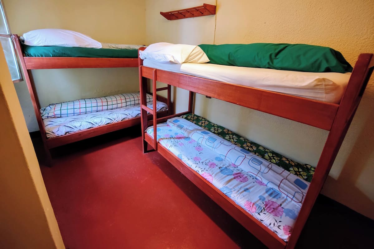 A room with two bunk beds, each with a mattress and pillow. There is a shelf on the wall above the beds.