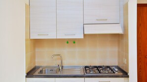 Une cuisine équipée d’un évier en acier inoxydable, d’une cuisinière à gaz et de meubles blancs.
