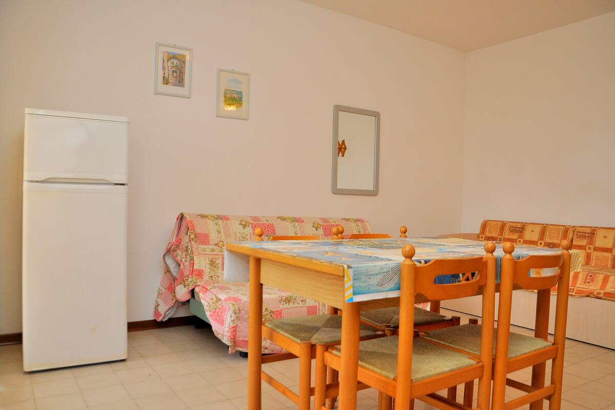 Een knusse, kleine kamer met een eettafel, stoelen, een bank en een koelkast.