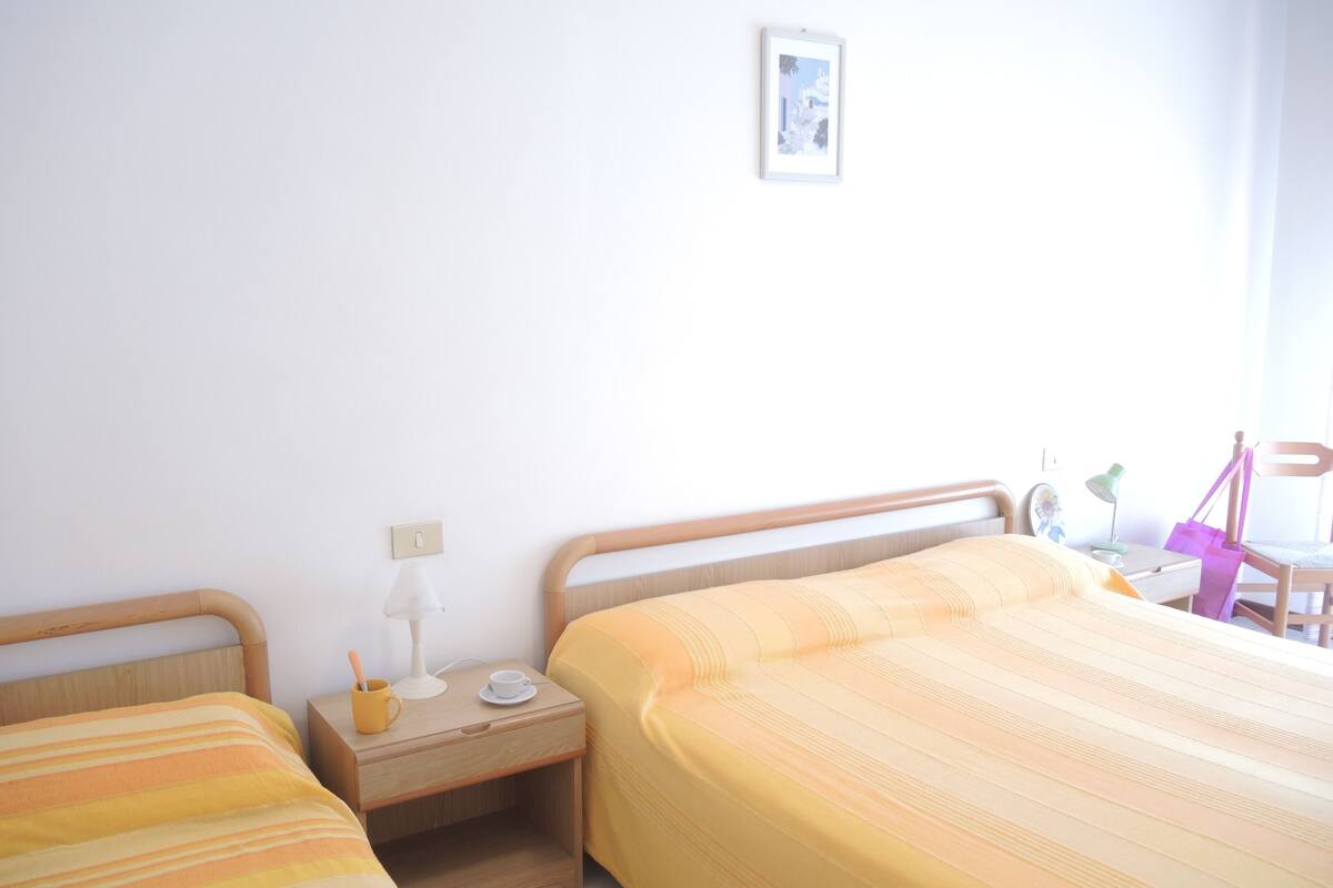 Een slaapkamer met twee bedden, een nachtkastje, een lamp, een stoel en een klein tafeltje met een lamp en een tas.
