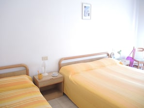 A bedroom with two beds, a nightstand, a lamp, a chair, and a small table with a lamp and a bag. - Appartamenti Tonin (San Michele al Tagliamento)