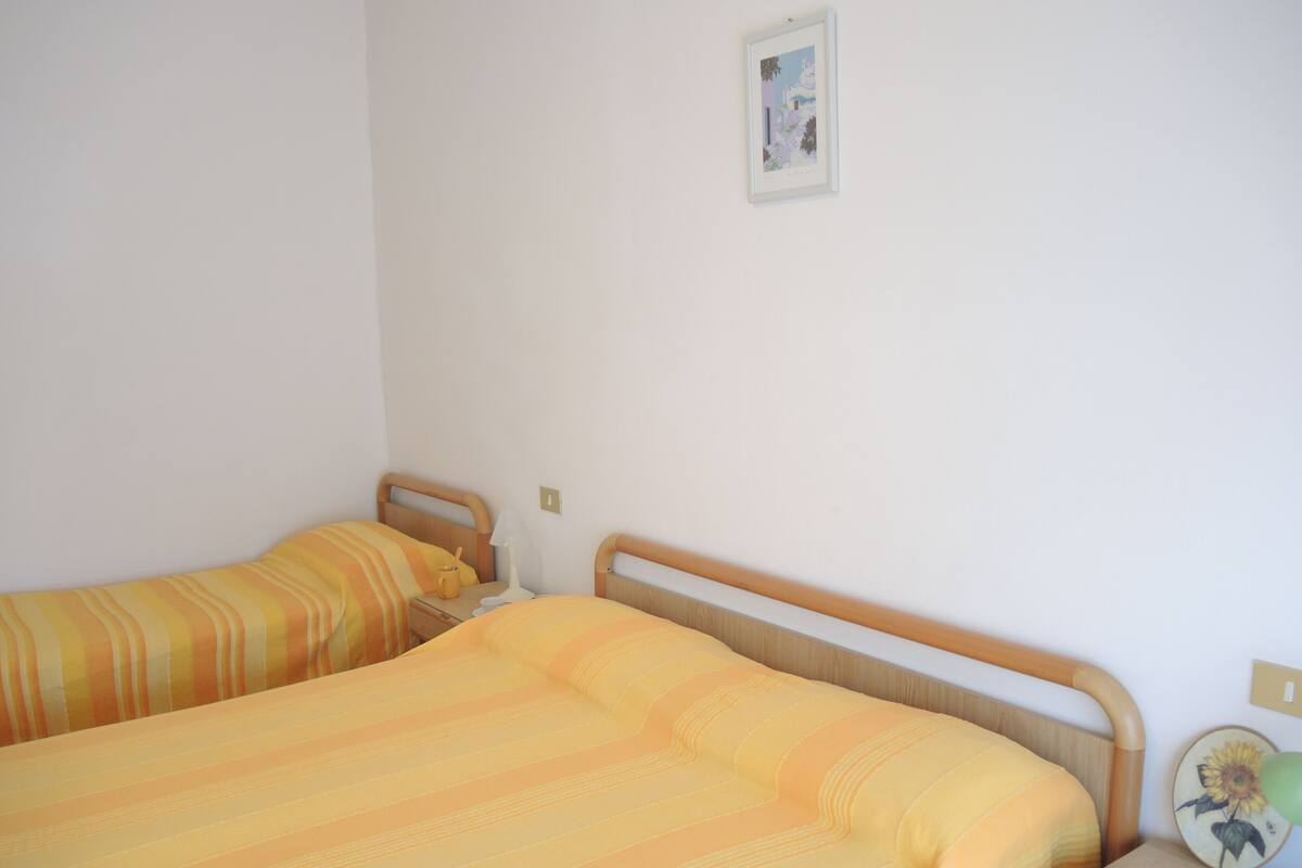 Een kamer met twee bedden, elk voorzien van gestreept beddengoed, een nachtkastje met een lamp en een aan de muur hangend schilderij.