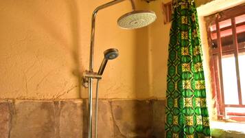 Een douche met een handdouche en een vaste douchekop, een gordijn met een groen patroon, en een stenen muur.