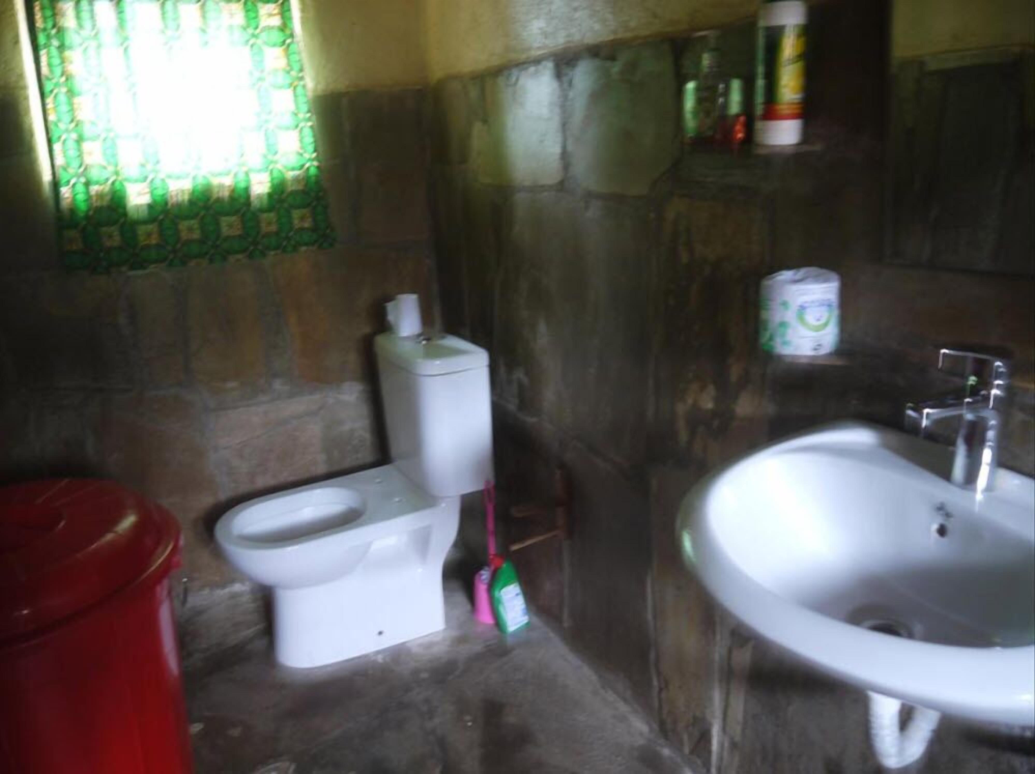 A bathroom with a toilet, sink, and a red trash bin.