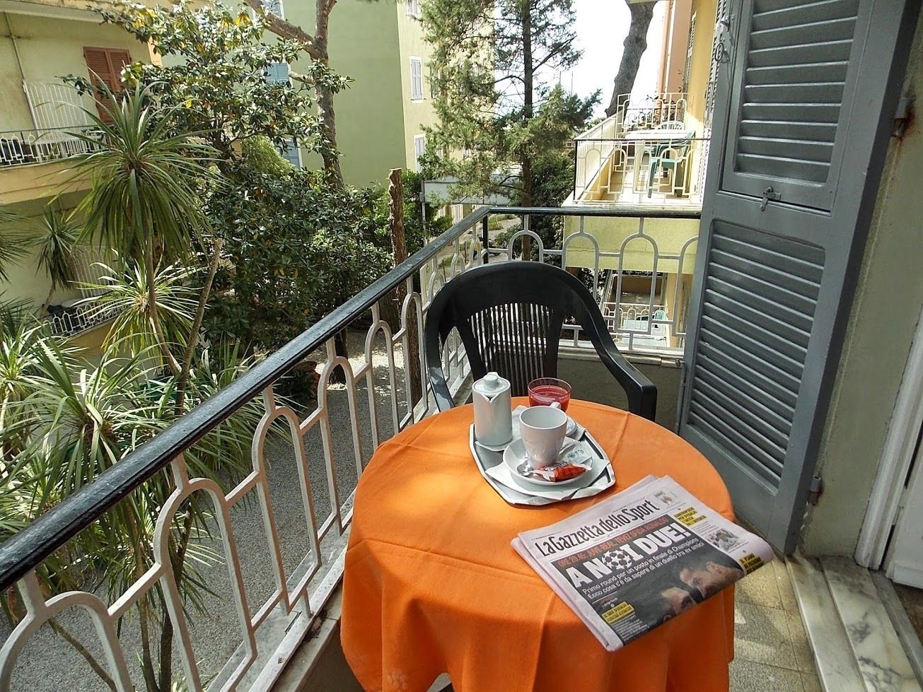 A balcony with a round table set for two, featuring a newspaper, a cup, and a plate with food.