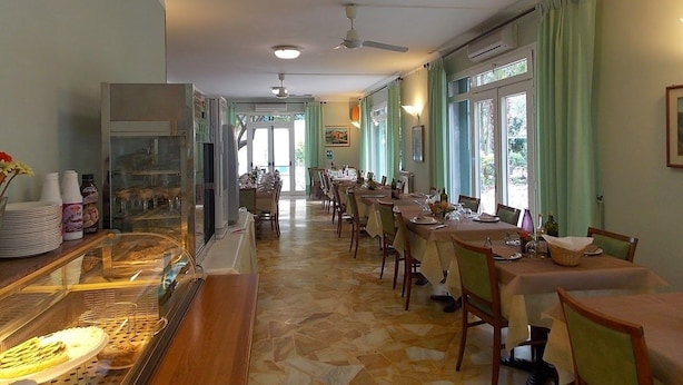 A dining area with multiple tables and chairs, a bakery display case, and a ceiling fan. - Hotel Arco del Sole (Lavagna)