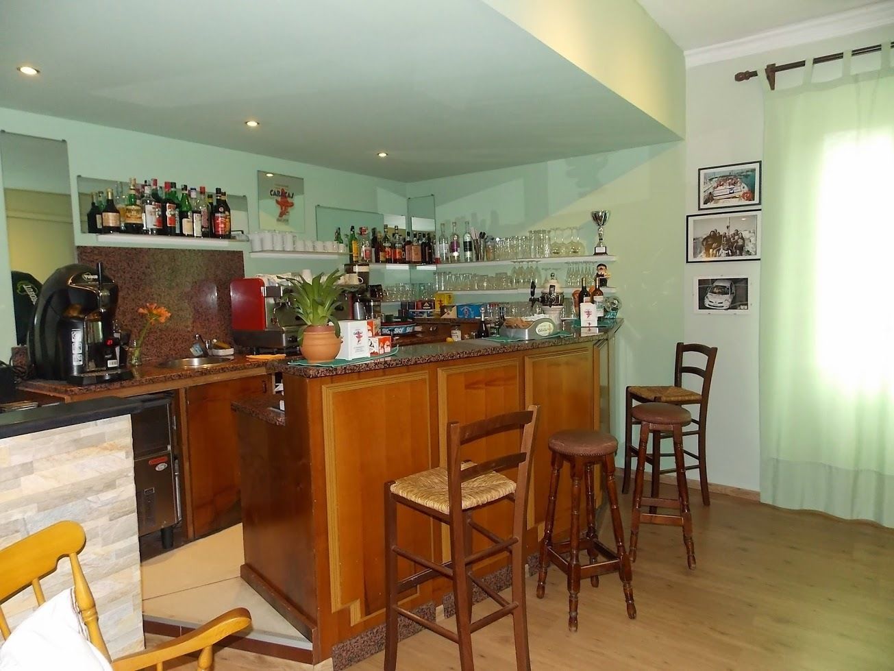 A bar area with a wooden counter, bar stools, and a variety of bottles and glasses.