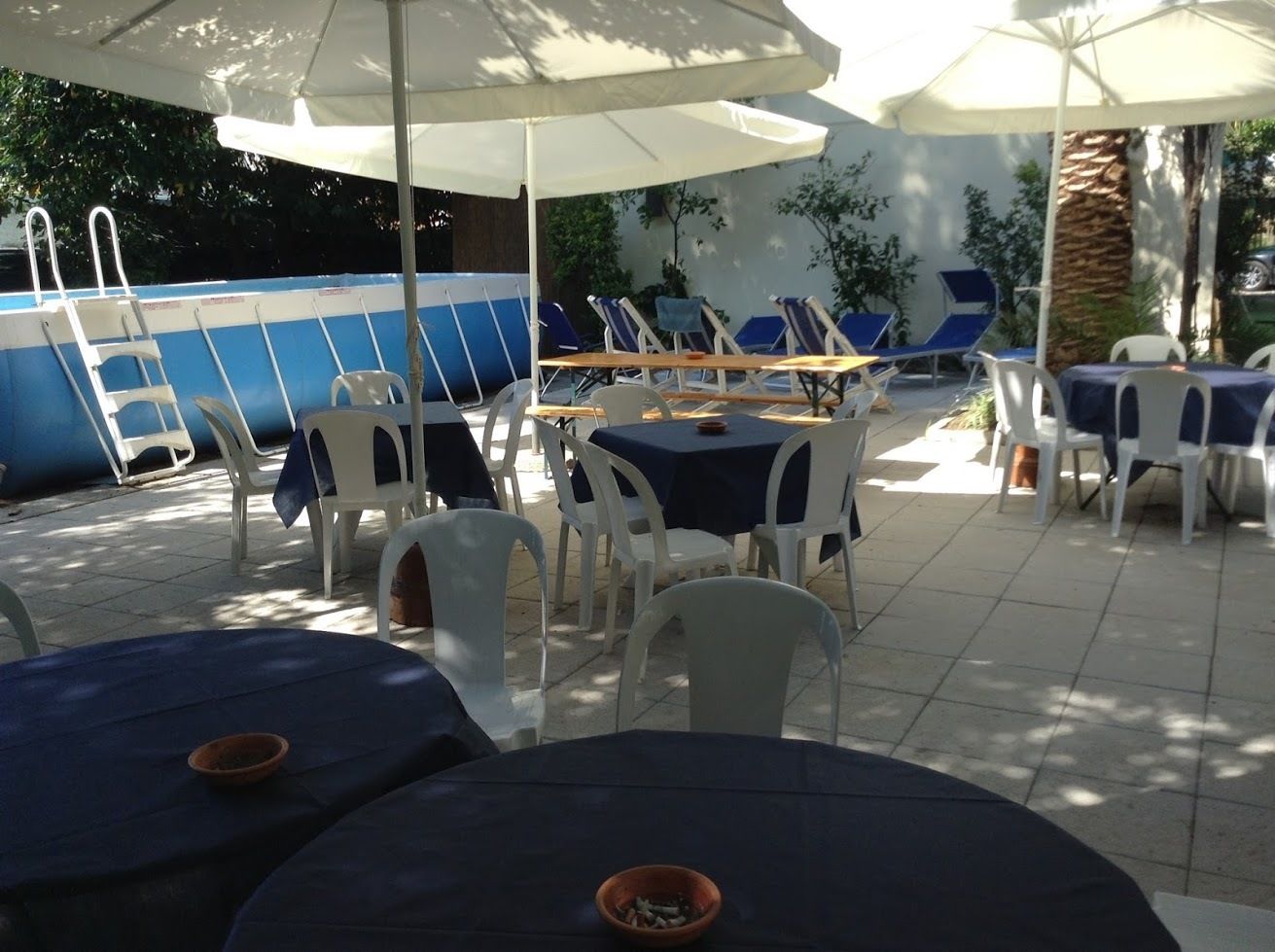 An outdoor patio with tables and chairs, a pool, and umbrellas.