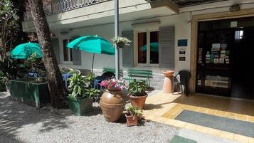 L'ingresso di un edificio con pavimento piastrellato, piante in vaso, un ombrello verde e una panchina.