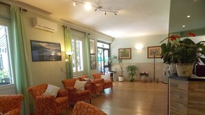 A spacious lobby with patterned orange chairs, a reception desk, potted plants, and artwork on the walls. - Hotel Arco del Sole (Lavagna)