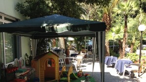 A covered outdoor play area with a small playhouse, tables, and chairs. - Hotel Arco del Sole (Lavagna)