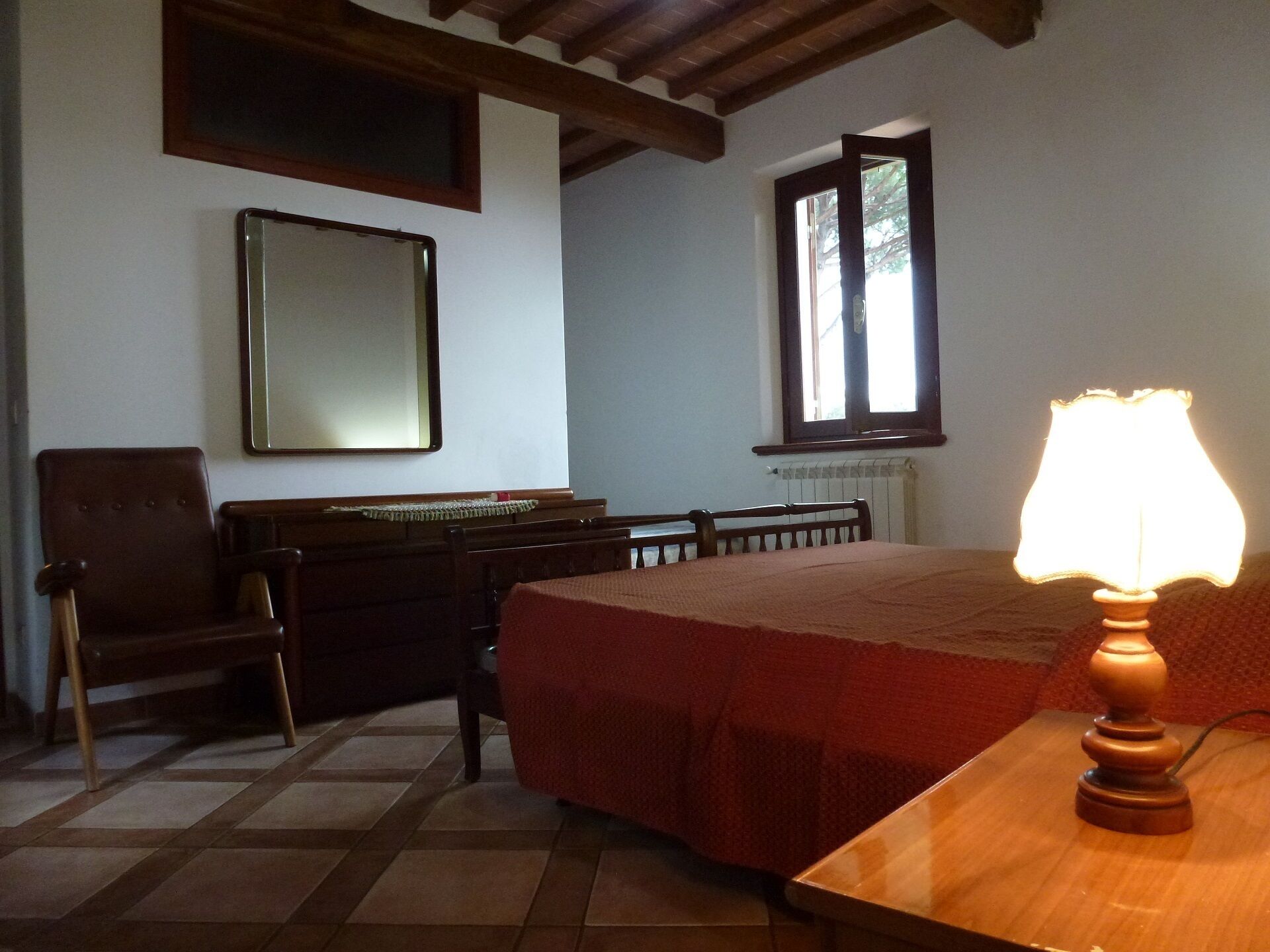 A bedroom with a bed, a chair, a desk, a lamp, a mirror, and a window.