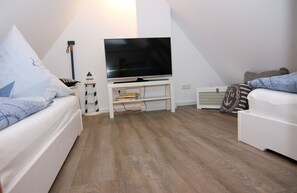 Una sala moderna con un televisor de pantalla plana sobre un soporte blanco, un sofá blanco y un segundo sofá blanco con cojines estampados.