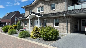Un edificio residencial de dos pisos con fachada de ladrillo, un porche cubierto y un camino de entrada con arbustos decorativos.