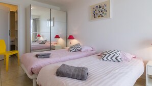 Ein Schlafzimmer mit zwei Betten, einem Spiegel, einem gelben Sessel und einem Nachttisch mit einer Lampe.