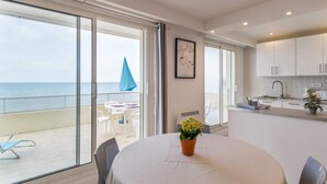 Eine moderne Küche mit weißen Schränken, eine Essecke mit Tisch und Stühlen und Meerblick durch große Schiebetüren.