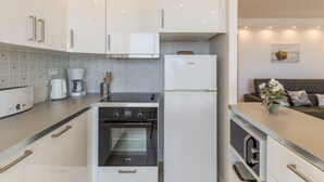 Eine moderne Küche mit weißen Schränken, einem Backofen, einem Kühlschrank und einer Kaffeemaschine.