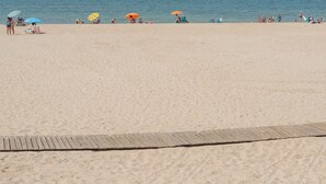 Une plage avec une promenade en bois, des gens se détendant sous des parasols, et l’océan en arrière-plan.