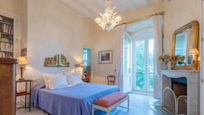 Une chambre à coucher comprenant un lit, un banc, une cheminée, un lustre et une bibliothèque.