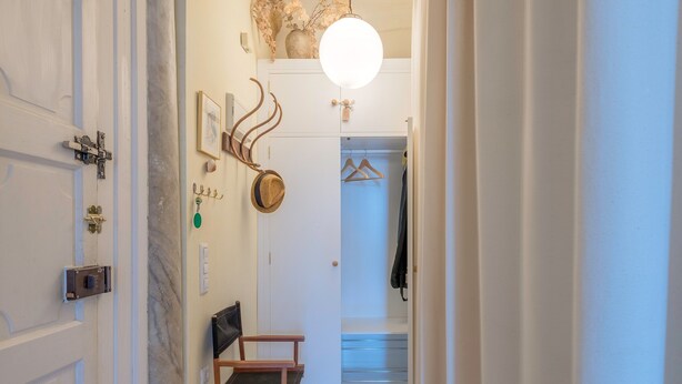 Een gang met een houten stoel, kapstok en een hangende hoed.