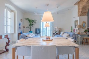 Une pièce spacieuse comprenant une grande table à manger en marbre, deux canapés, un téléviseur et une plante en pot.