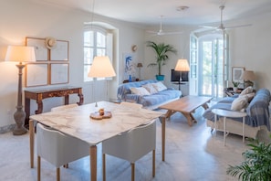 Un vaste espace de vie comprenant une table en marbre, un canapé, un téléviseur et un ventilateur de plafond.