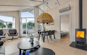 Una sala de estar moderna con una gran mesa de comedor, asientos cómodos, una chimenea y ventanas amplias que ofrecen vistas al exterior.
