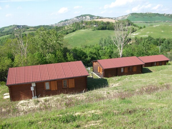A wooden cabin with a red roof, surrounded by green hills and trees. - La Luna sul Trebbio (Modigliana)
