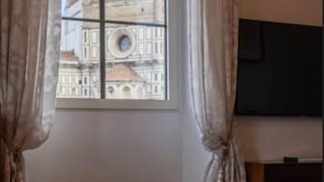 A room with a large window, curtains, a flat-screen TV, and a wooden floor.