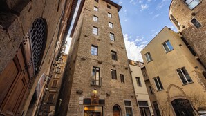 Uma rua estreita com edifícios históricos de pedra, incluindo um edifício de destaque com uma placa que diz 'ANTICO ALBERGO'.