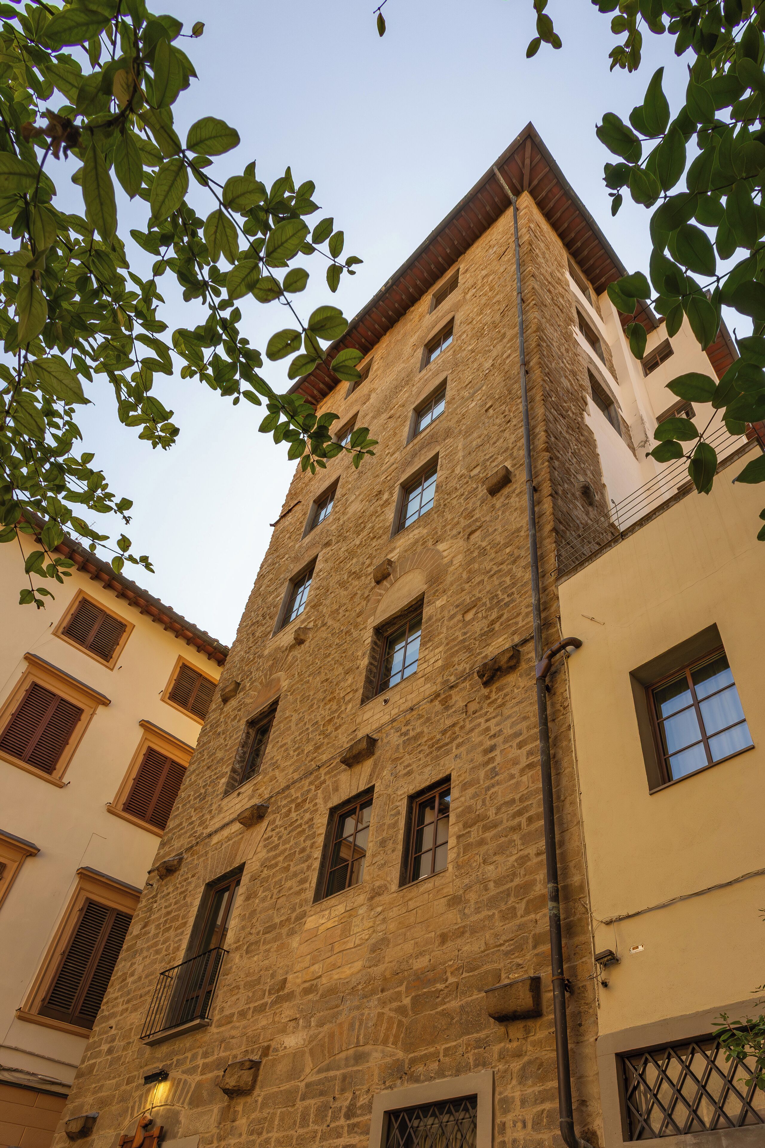 Un edificio de varios pisos de piedra con numerosas ventanas y balcones, rodeado de otros edificios.