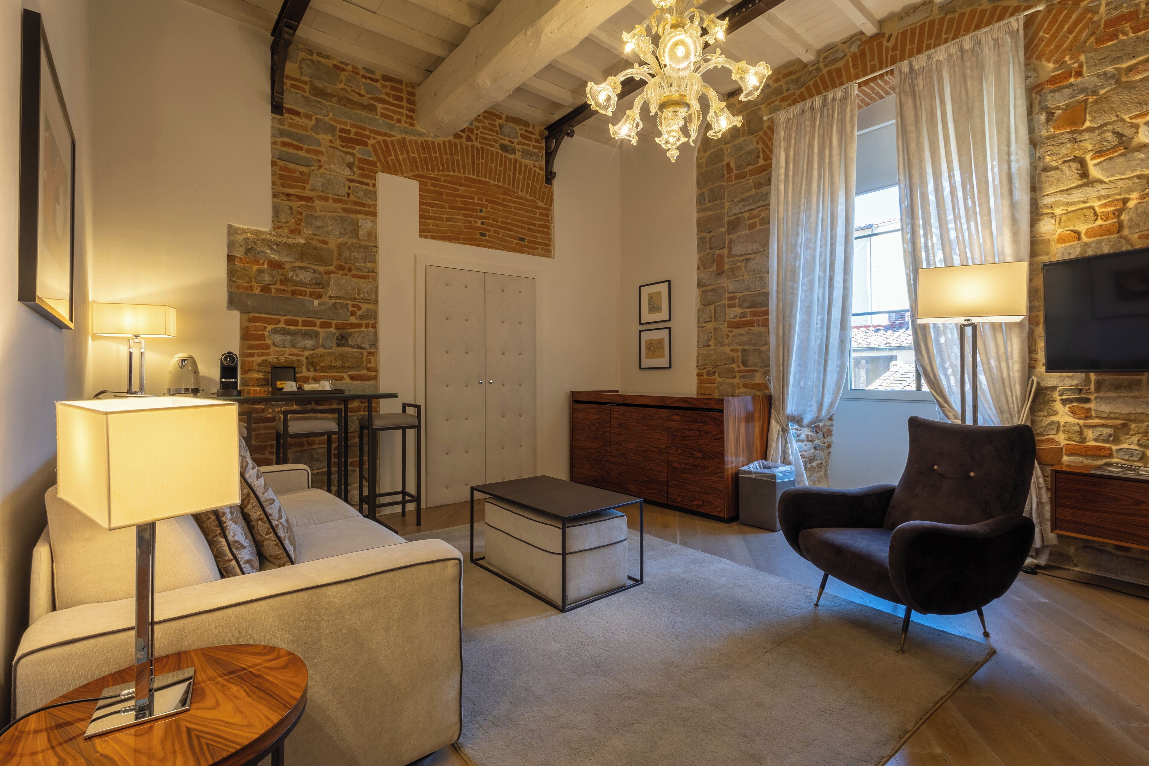 A cozy living room with a stone wall, a chandelier, a sofa, a chair, a coffee table, and a TV.