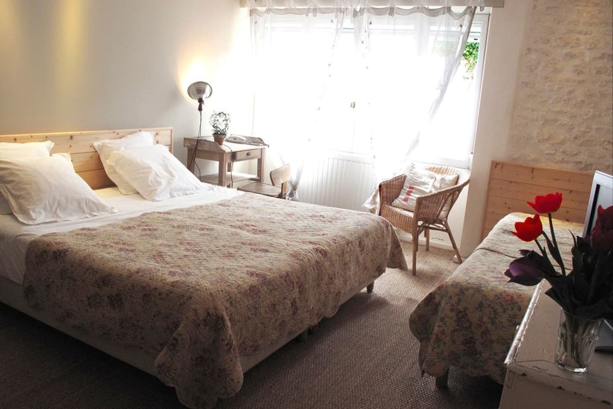 Ein Schlafzimmer mit einem großen Bett, einem Schreibtisch und einem Stuhl. Ein Fenster mit Vorhängen und eine Heizung sind ebenfalls vorhanden.