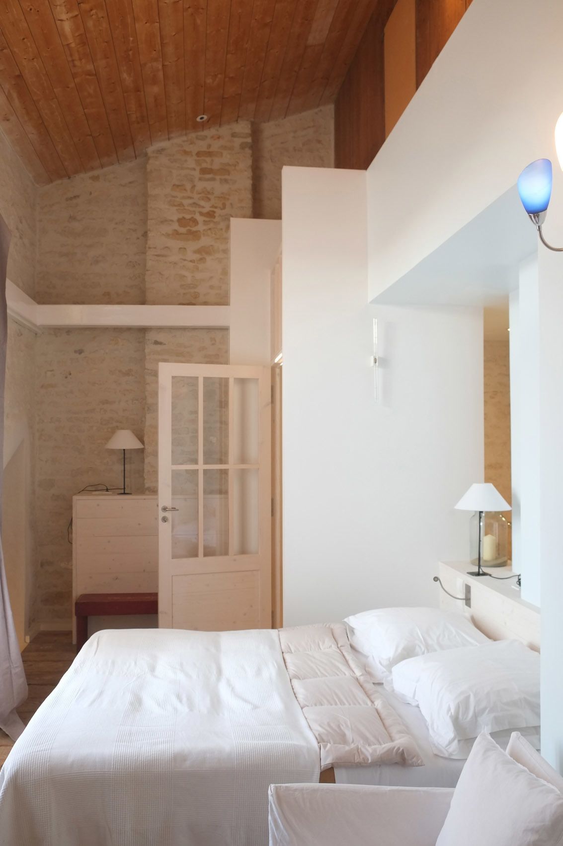 Een slaapkamer met twee bedden, een houten plafond, een stenen muur en een witte deur.