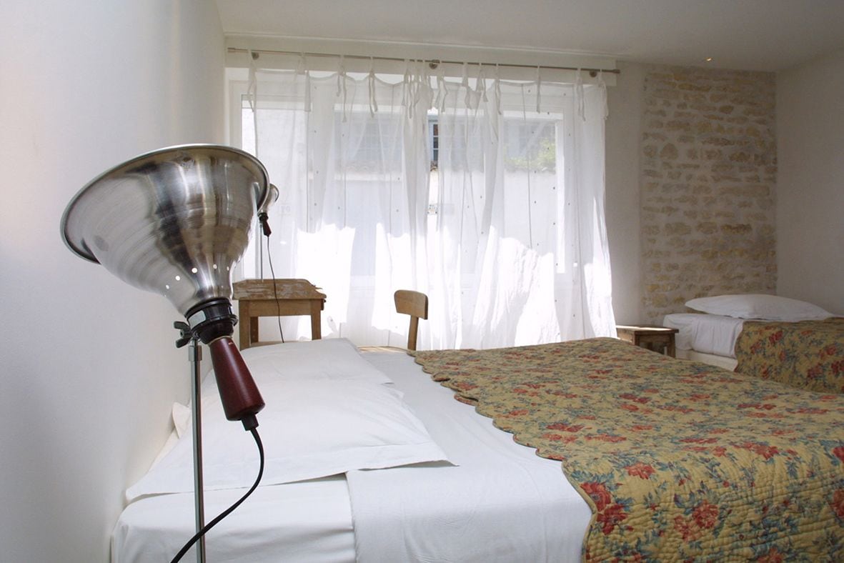 Ein Zimmer mit einem Bett, einer Lampe, einem Sessel und einem Fenster mit Vorhängen.