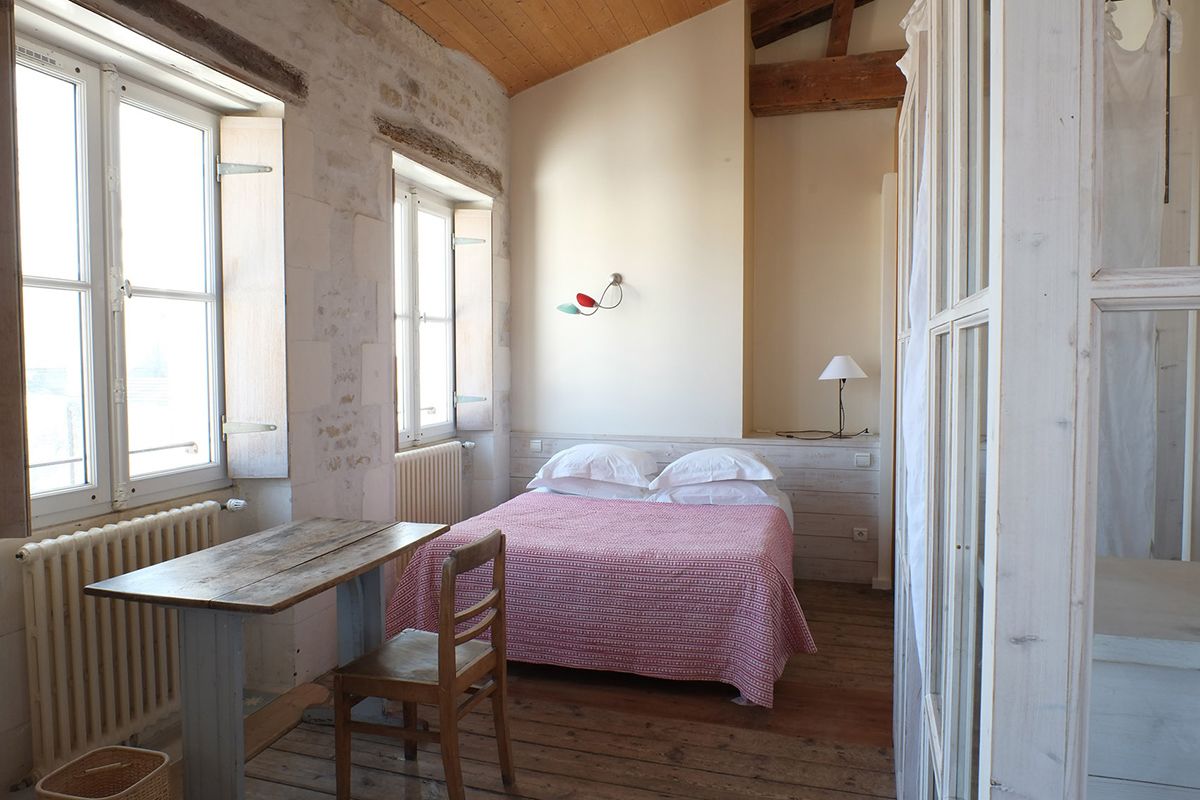 Ein Zimmer mit einem Bett, einem Tisch und einem Stuhl. Es gibt ein Fenster und eine Heizung.