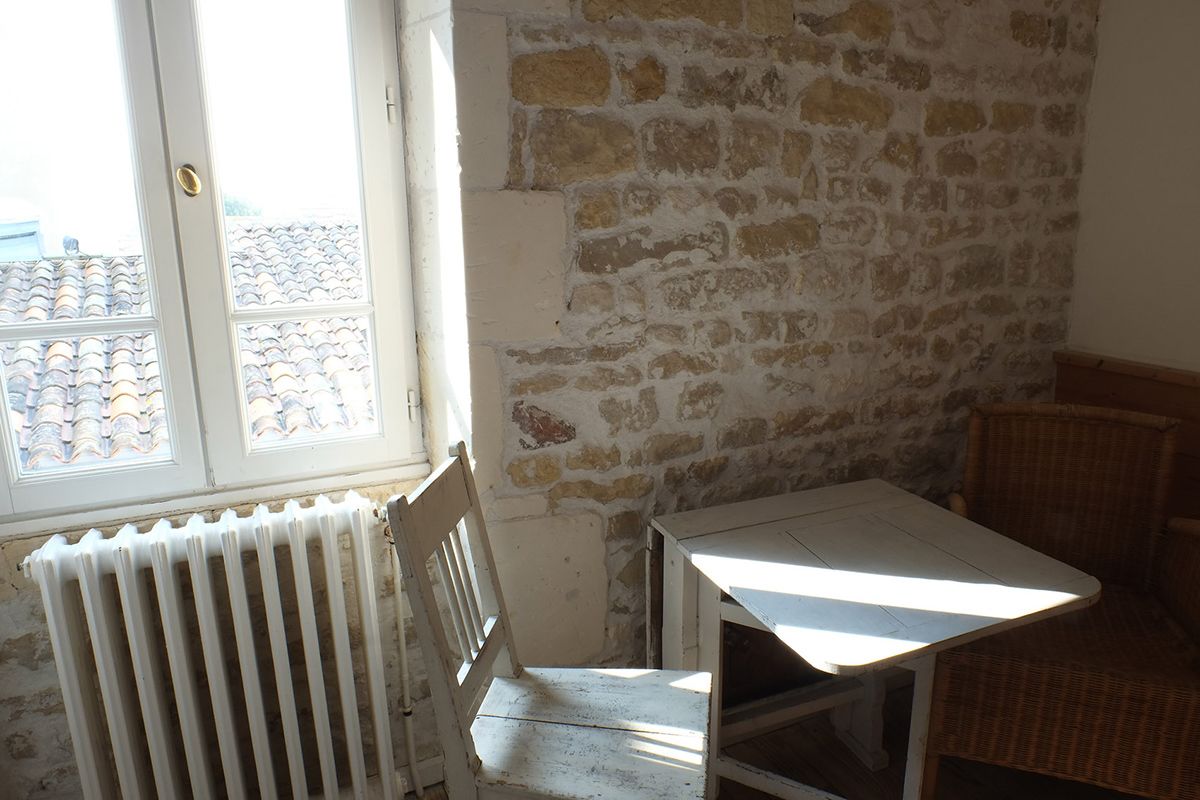 Ein Zimmer mit Stehwand, Heizkörper, Fenster mit Rollläden und einem Korbstuhl.