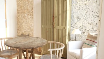 Une pièce au décor rustique, avec une table ronde en bois, deux chaises en osier, un canapé blanc et une armoire verte.