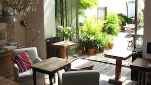 A cozy interior with a dining area, a comfortable seating area, and a view of the garden through large windows. - Hôtel Le Sénéchal (Ars-en-Re)